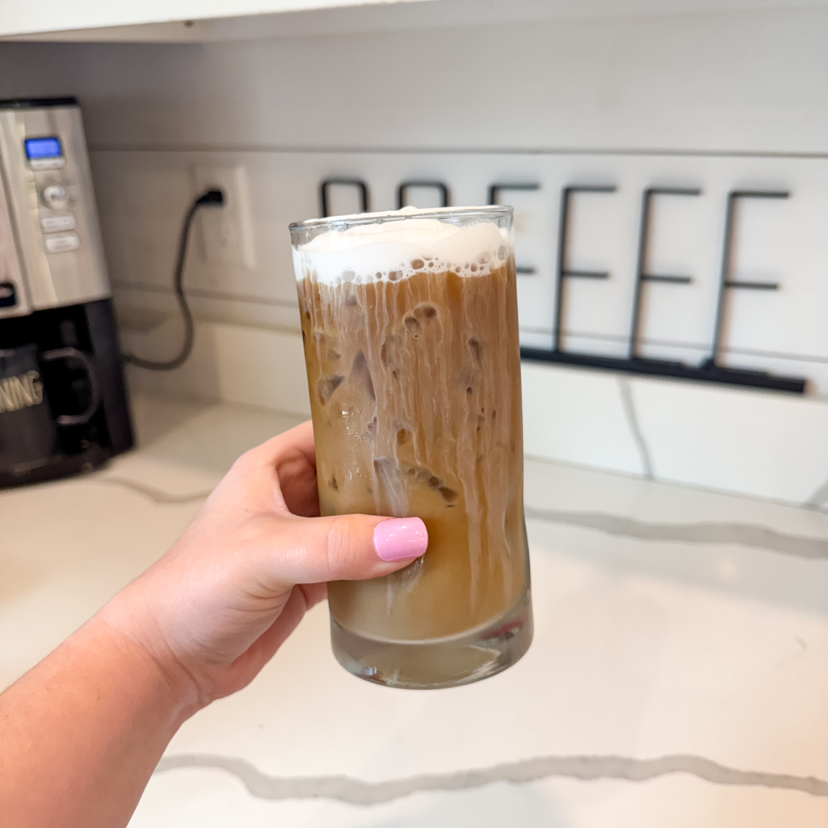 hand holding a clear glass with an iced latte