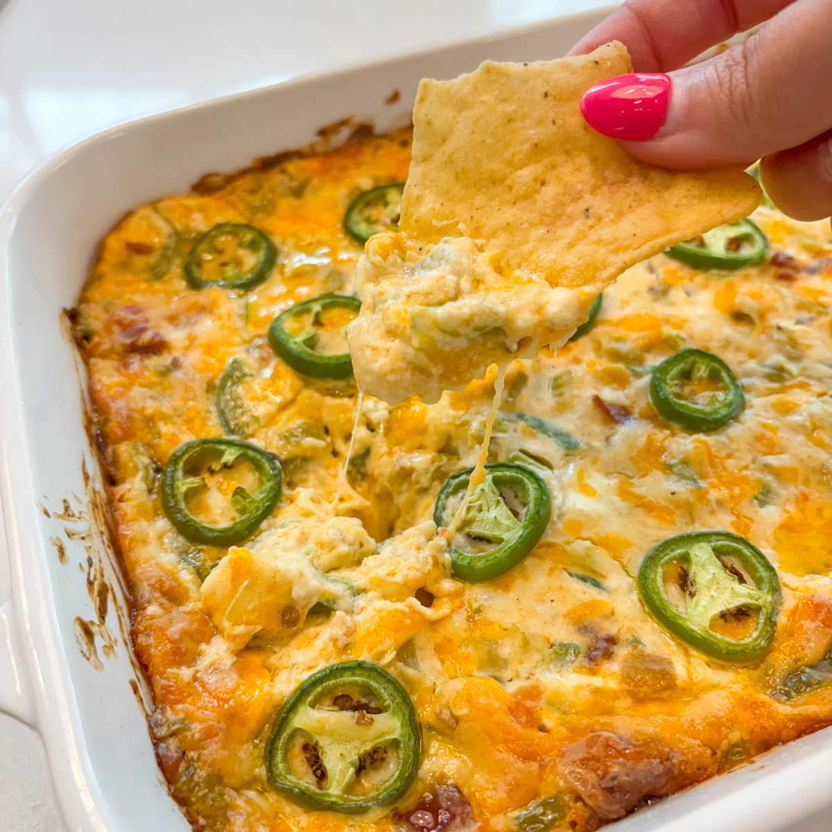 tortilla chip being dipped in jalapeno popper dip