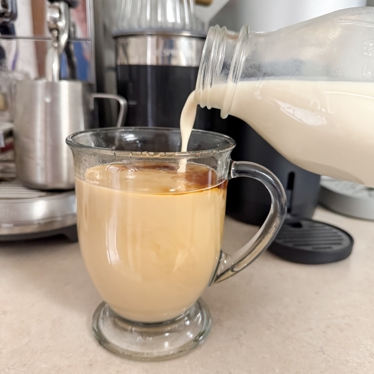 pouring coffee creamer into a clear glass of coffee